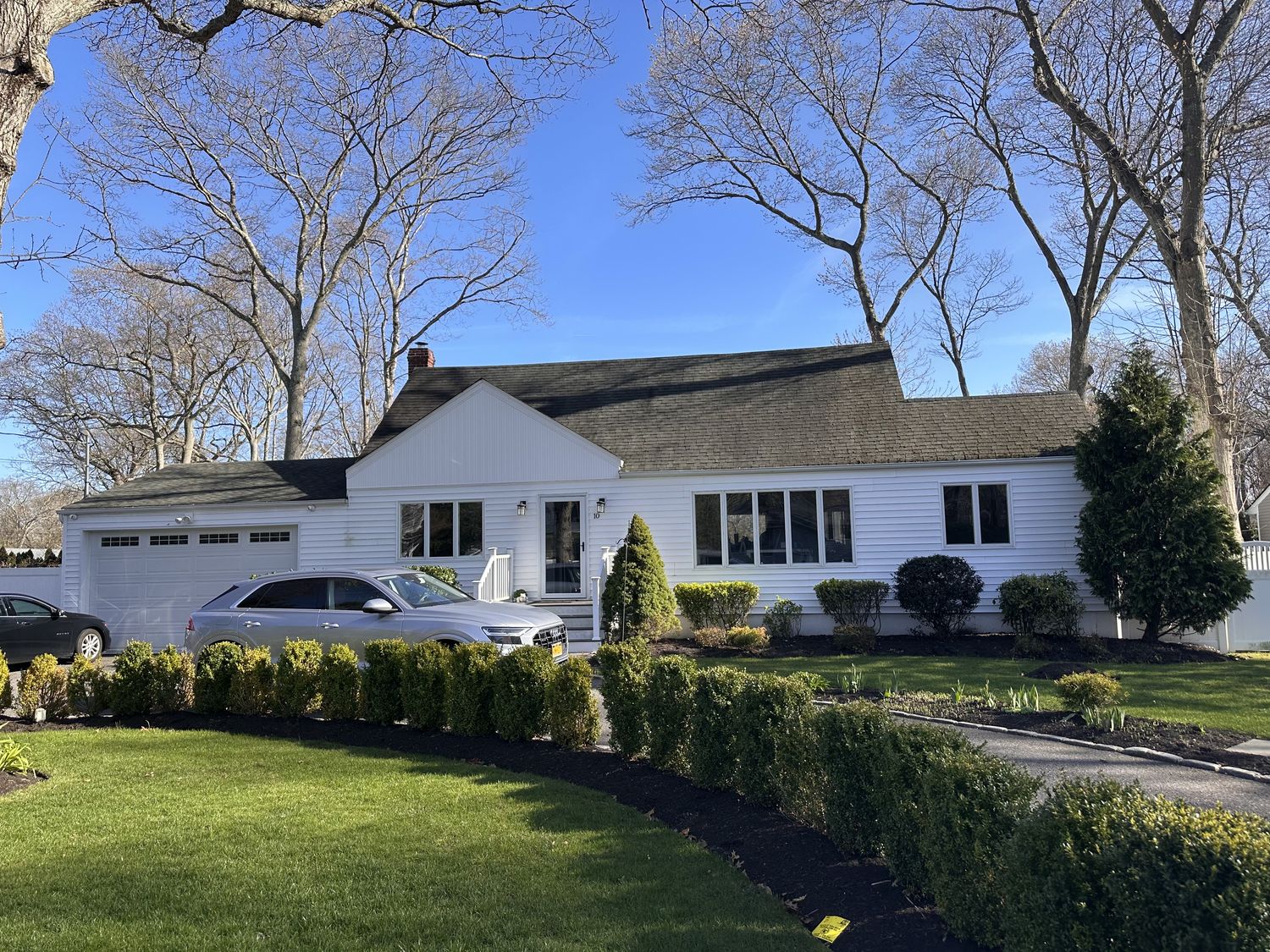 White Cape Cod home with an attached garage and mature landscaping in Nassau County, Long Island