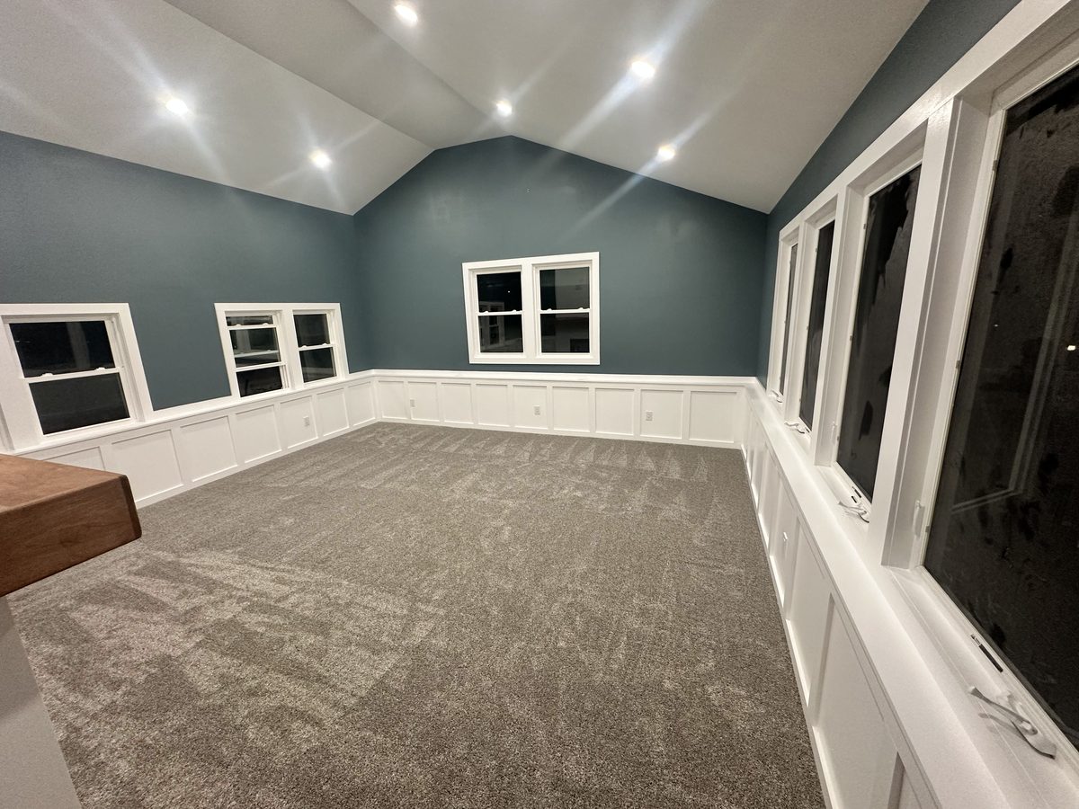 Finished dormer interior with a vaulted ceiling, wainscoting, and multiple windows created by a second-story conversion on Long Island