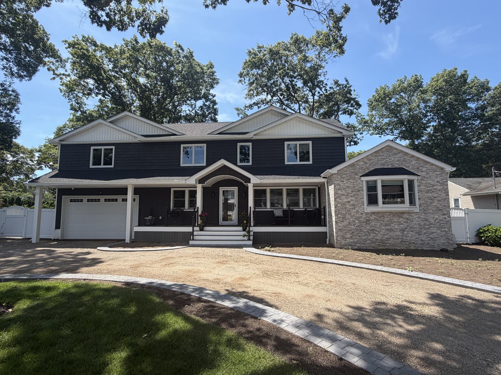 Completed second-story addition and home extension by Meigel on a Long Island home, with navy shake siding, a covered front porch, and a stone-veneer wing